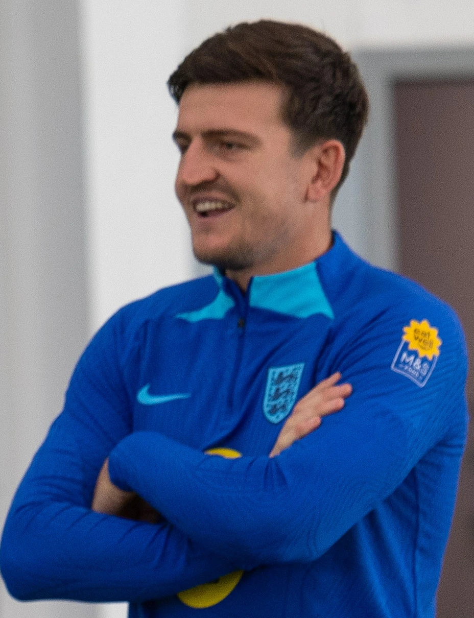 Harry Maguire in a Manchester United training top, smiling with arms crossed
